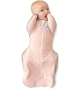Gray baby swaddle with white pom-pom trim and full-length zipper. Star-shaped design restricts arm movement. Small blue logo visible on chest area.