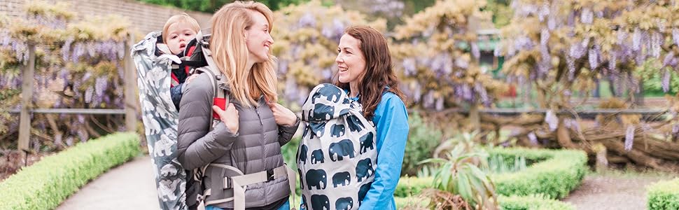 Person wearing a grey vest holding a fabric with blue elephant pattern, likely a baby carrier or wrap, in an outdoor setting.