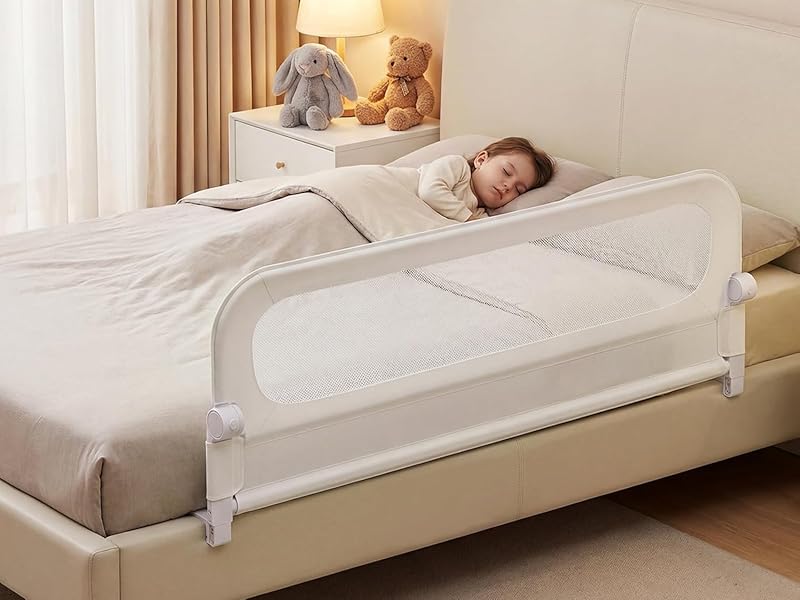 White bed rail safety guard installed on beige bed frame with child sleeping. Guard features vertical bars and extends along mattress edge for fall prevention.