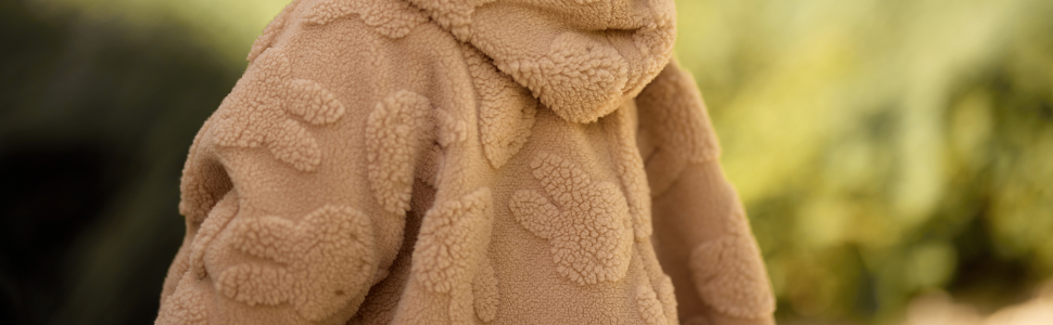 Close-up of tan/beige woven fabric texture with tight weave pattern. Natural fiber material shown in outdoor lighting with blurred green background.