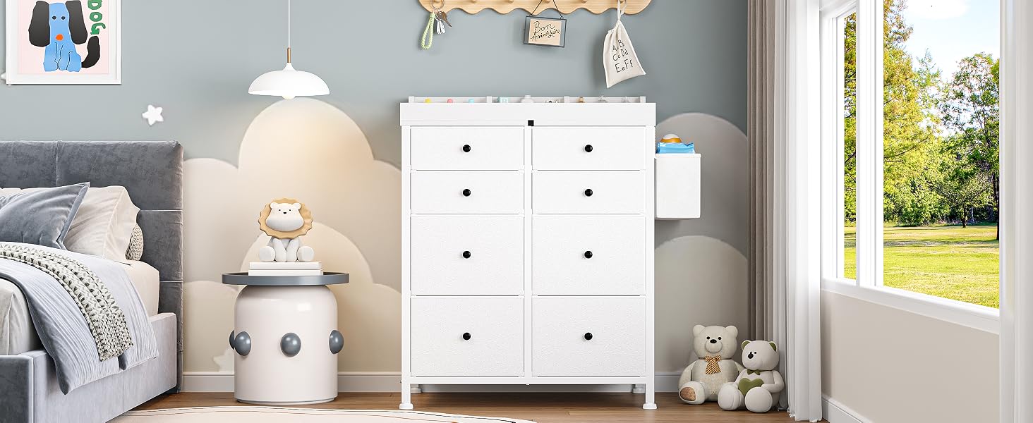 Bedroom nightstand with white multi-drawer dresser, ceramic decorative items, table lamp, potted plant, and window with outdoor view. Minimalist, light-toned bedroom styling.