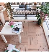 Overhead view of outdoor patio space with gray tile flooring, white table, black cushioned chairs, potted plants, and motorcycle against railing.